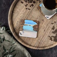 Load image into Gallery viewer, Corkwood underside, glossy finish on top. 1 or 4 pc sets. 9.5x9.5cm Penguins marching from a turquoise ocean up a rocky beach