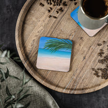 Load image into Gallery viewer, Corkwood underside, glossy finish on top. 1 or 4 pc sets. 9.5 x 9.5cm. Palm leaves and a tranquil turquoise beach