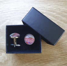 Load image into Gallery viewer, original artwork of a sunrise (in the form of the ANZAC Crest) with a silhouette of a soldier kneeling next to his horse drinking from his hat in a field of red and purple poppies on 16mm platinum cufflinks
