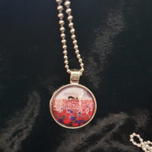 Load image into Gallery viewer, original artwork of a sunrise (in the form of the ANZAC Crest) with a silhouette of a soldier kneeling next to his horse drinking from his hat in a field of red and purple poppies on a 25mm silver coloured round pendant with a 60cm ball chain
